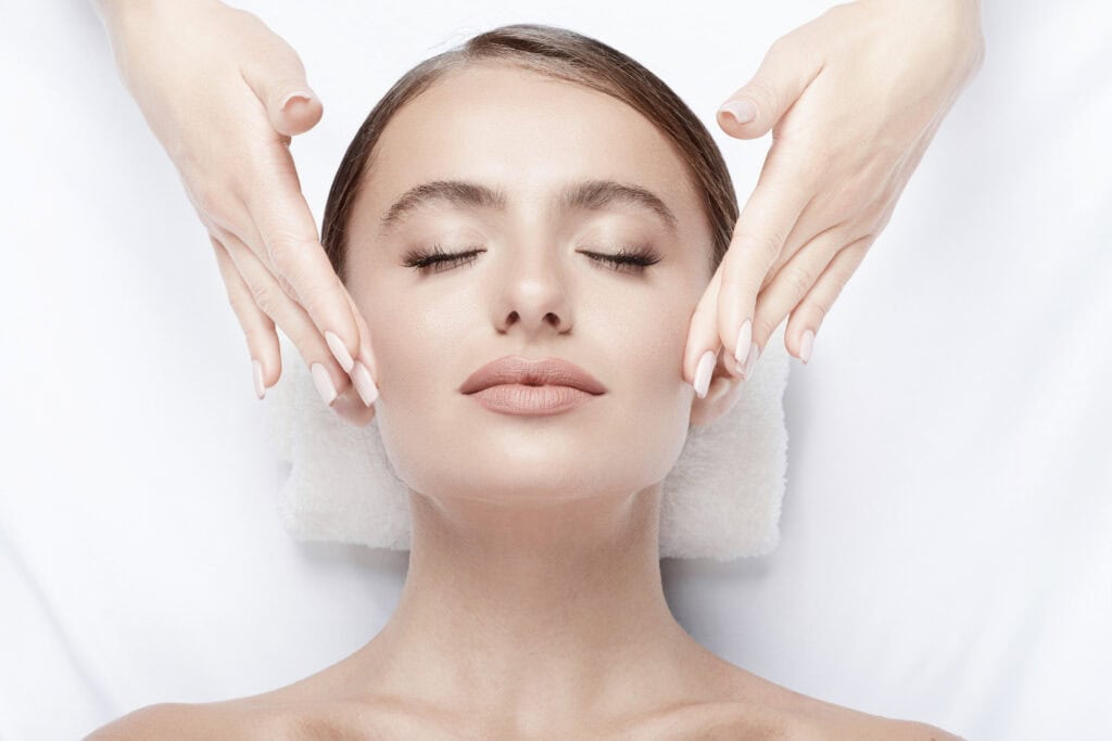 Woman receiving professional facial massage treatment with eyes closed, relaxed expression during skincare therapy session