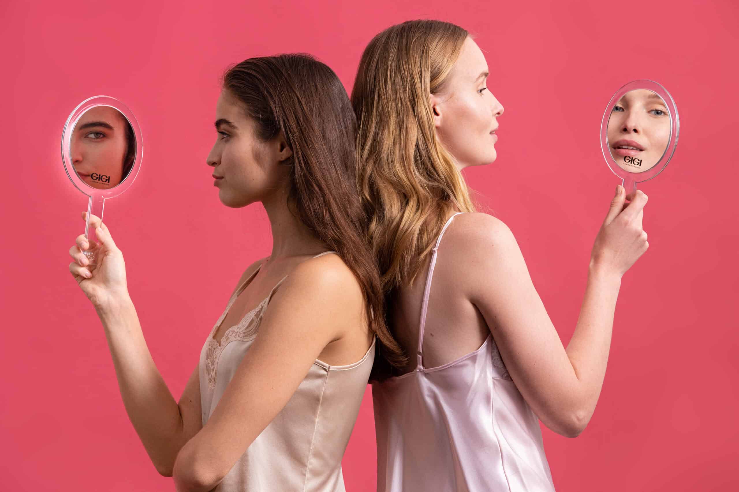 Two women examining their skin with GIGI branded mirrors during skincare routine